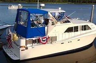 A white motor yacht with a Robie Canvas custom blue enclosure and bimini top, docked at a marina, decorated with patriotic bunting.