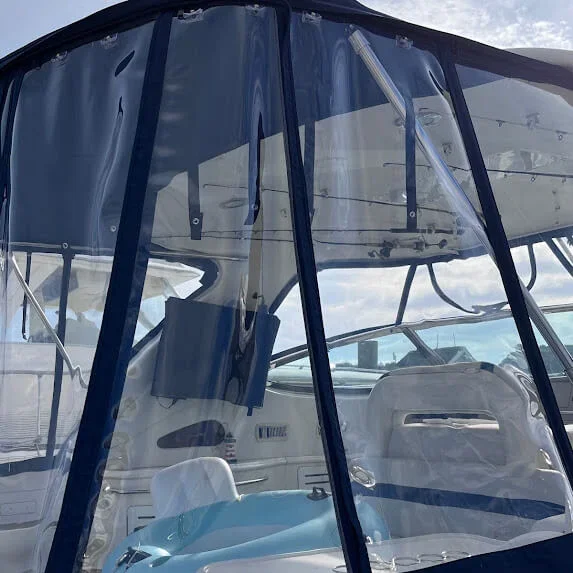 View of the interior of a boat, seen through a clear plastic custom enclosure made by Robie Canvas, with the steering wheel and seating visible.