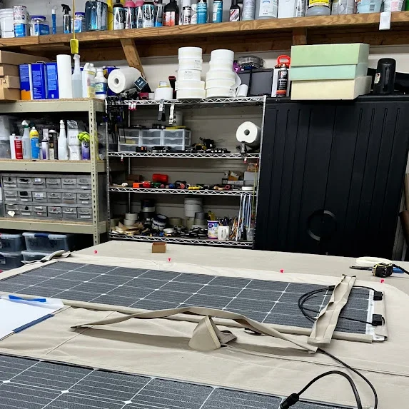 Workbench with solar panel components and tools in a workshop with shelves, storage bins, and supplies in the background.