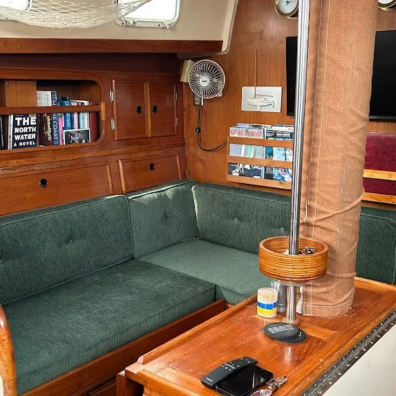 Interior of a boat with a green upholstered seating area completely refined by Robie Canvas, wooden cabinetry, a small desk with remote controls, a wall-mounted fan, and a book about North Water.