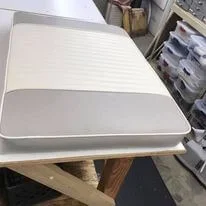 A white heated mattress pad on a wooden table in a room with storage shelves.