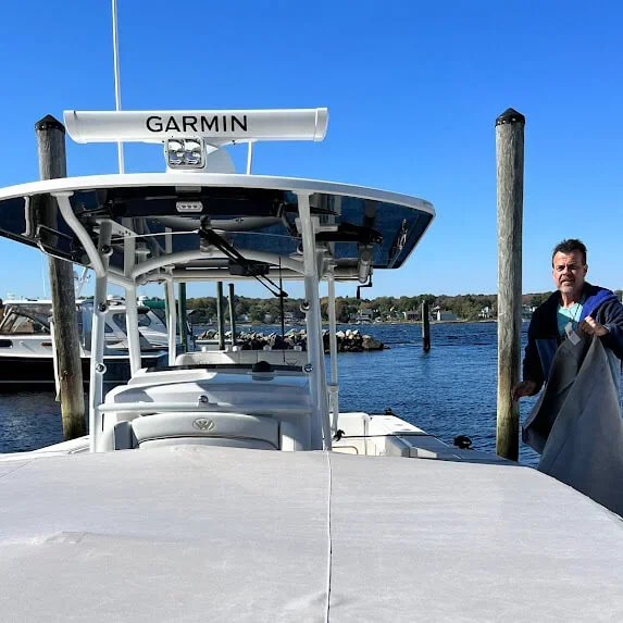 A white boat docked at a marina with a Garmin radar and a Robie Canvas employee standing on the dock proud of the bow cover he just installed.