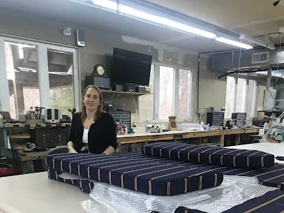 Woman in a black blazer standing next to multiple large padded cushions or mattresses on a table in a room with electronics and large windows.