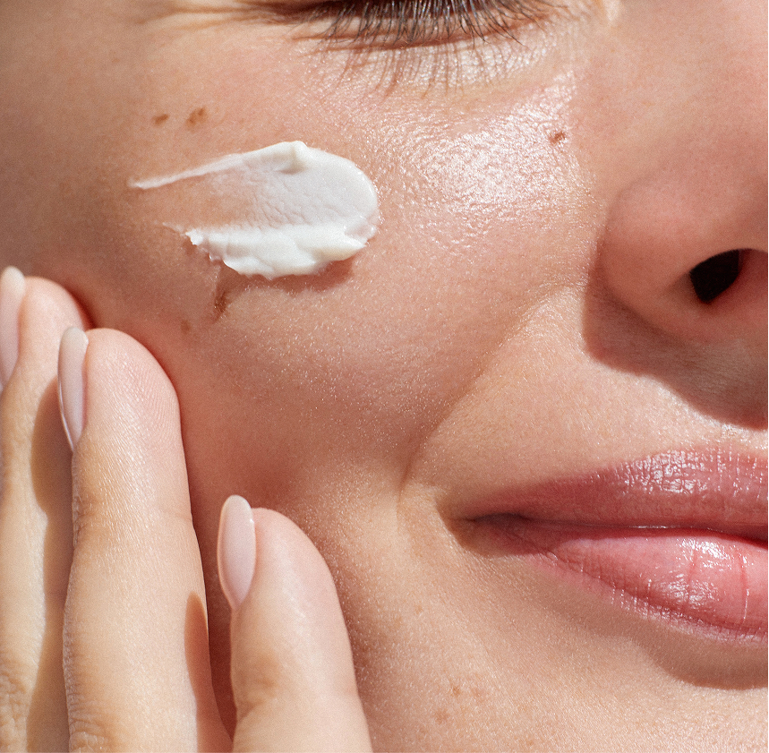 Close-up of a woman applying white cream or moisturizer to her face with her fingers.