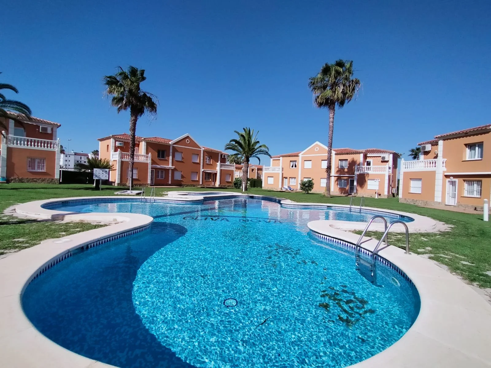 Piscina en un complejo de casas con palmeras y un cielo despejado.