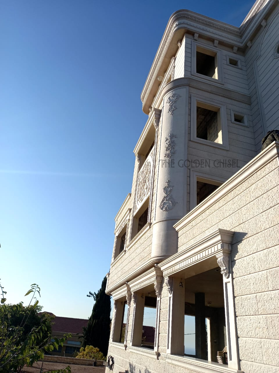واجهة جانبية لفيلا من الحجر الطبيعي مع أعمدة وشرفات أنيقة. Luxury stone villa exterior with classical columns and elegant balconies.