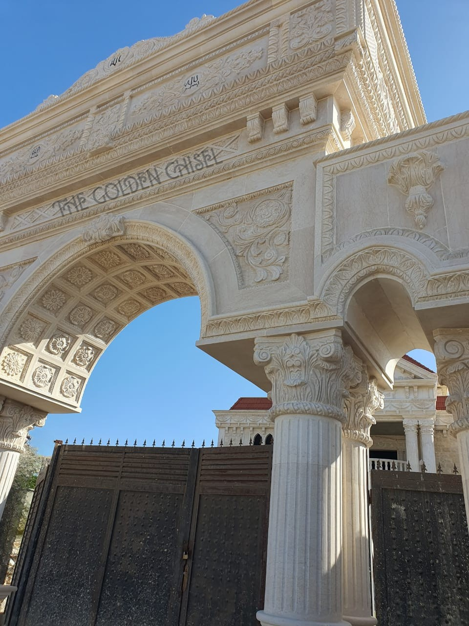 مدخل فيلا فاخر من الحجر الطبيعي مع قوس مزخرف وأعمدة ونقوش حجرية يدوية | Luxury natural stone villa entrance with an ornate arch, columns, and hand-carved stone details
