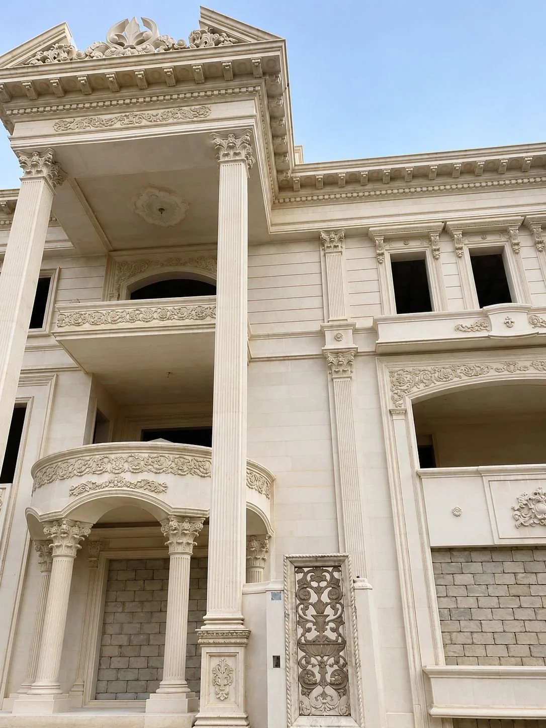 واجهة فيلا فاخرة من الحجر الطبيعي مع أعمدة وزخارف كلاسيكية منحوتة. Luxury natural stone villa facade with carved columns and classic ornate details.