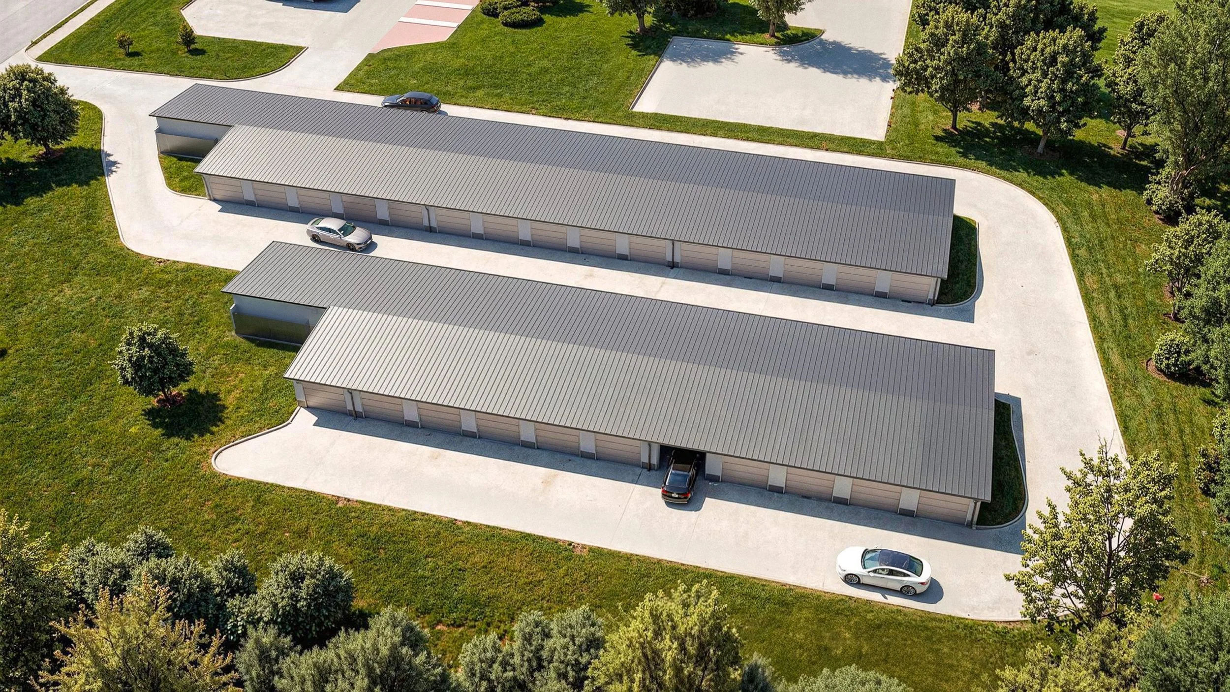 Légi felvétel egy garázs komplexumról: két hosszúkás garázsépület, parkoló autók, burkolt behajtók, zöld gyep és fák.