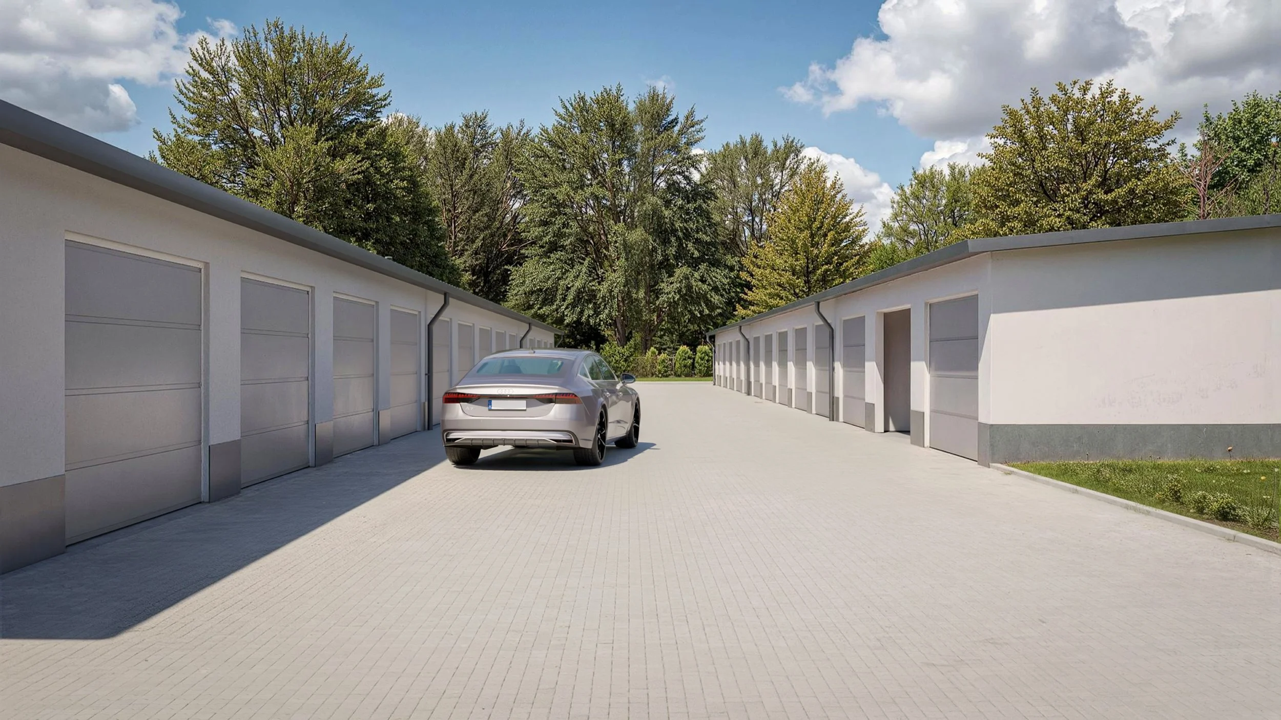 Ezüstszínű autó két garázs között parkol; háttérben fák és részben felhős ég.