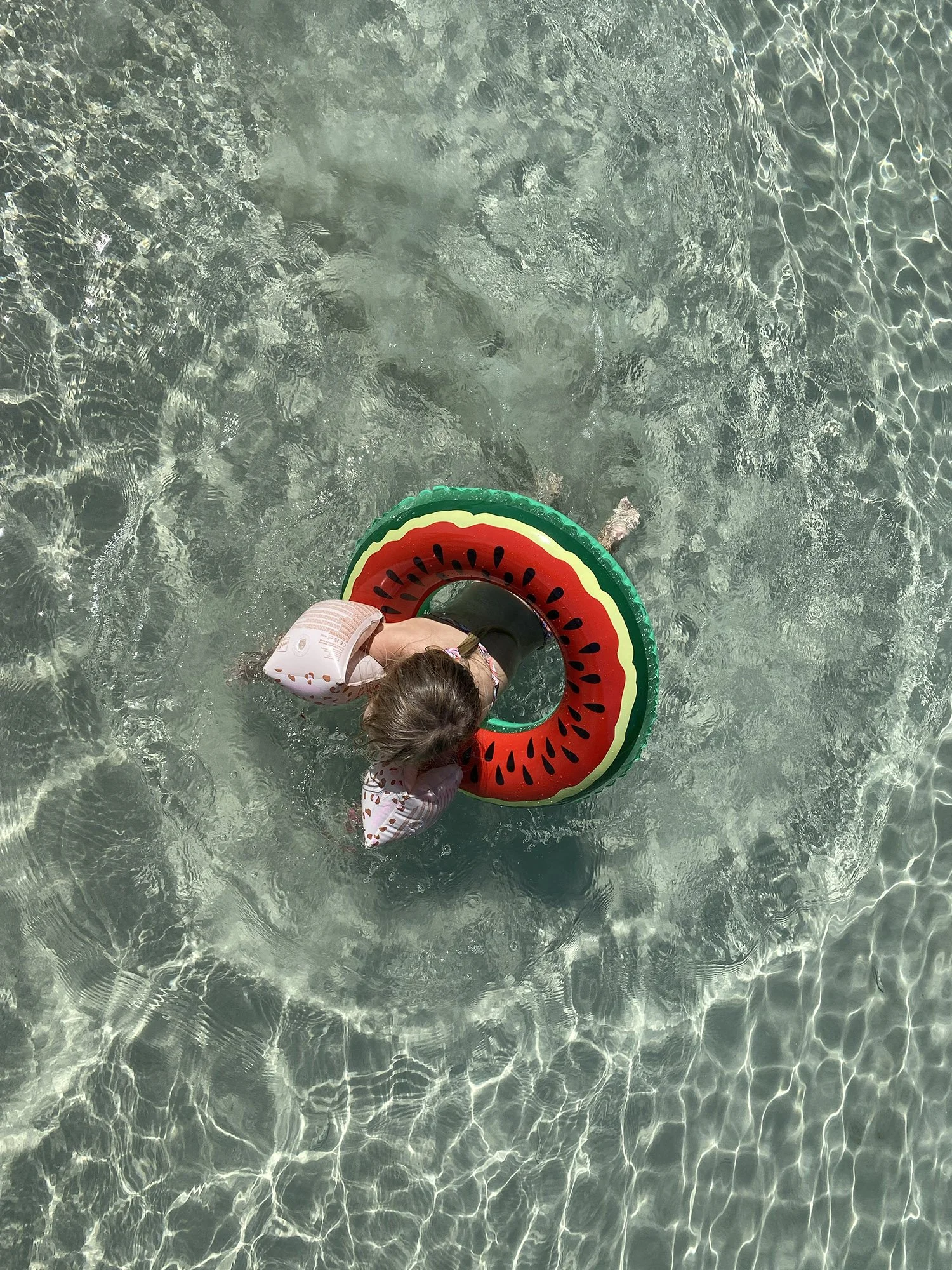 Kinderen in het water met een opblaasring in de vorm van een watermeloen.
