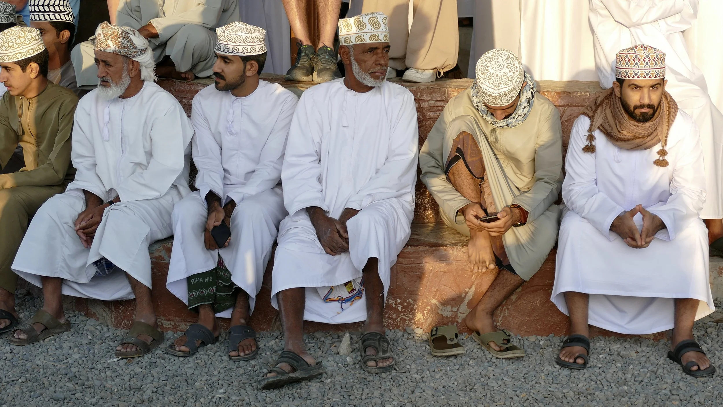 Groep Omaanse mannen in traditionele witte gewaden en geborduurde kumma-hoofddeksels, zittend op stenen treden.