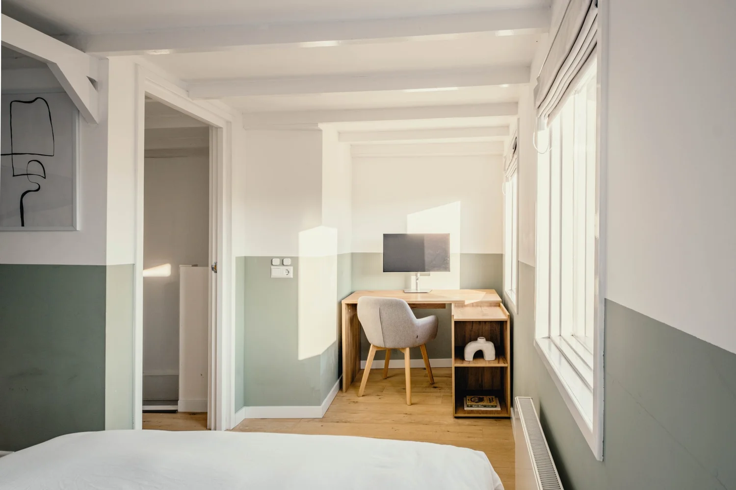 Minimalistische kamer met een werkplek bij het raam en een boekenkast.