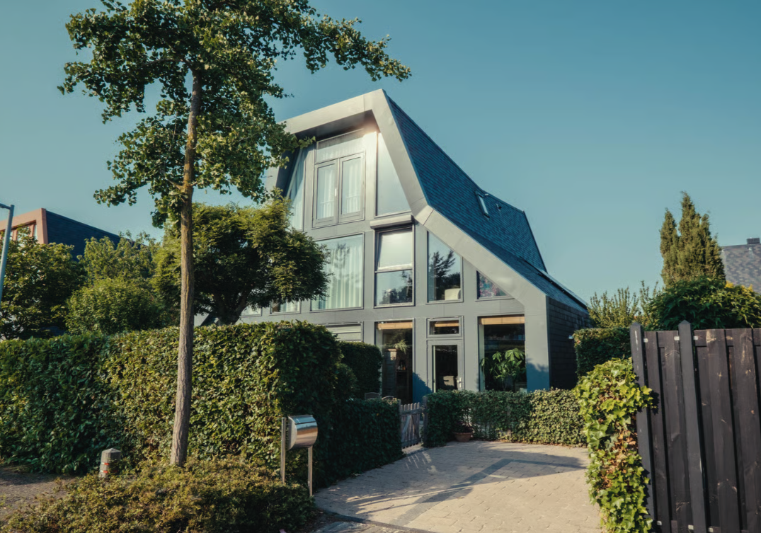 Modern huis met een schuine dakpartij, omgeven door groen.