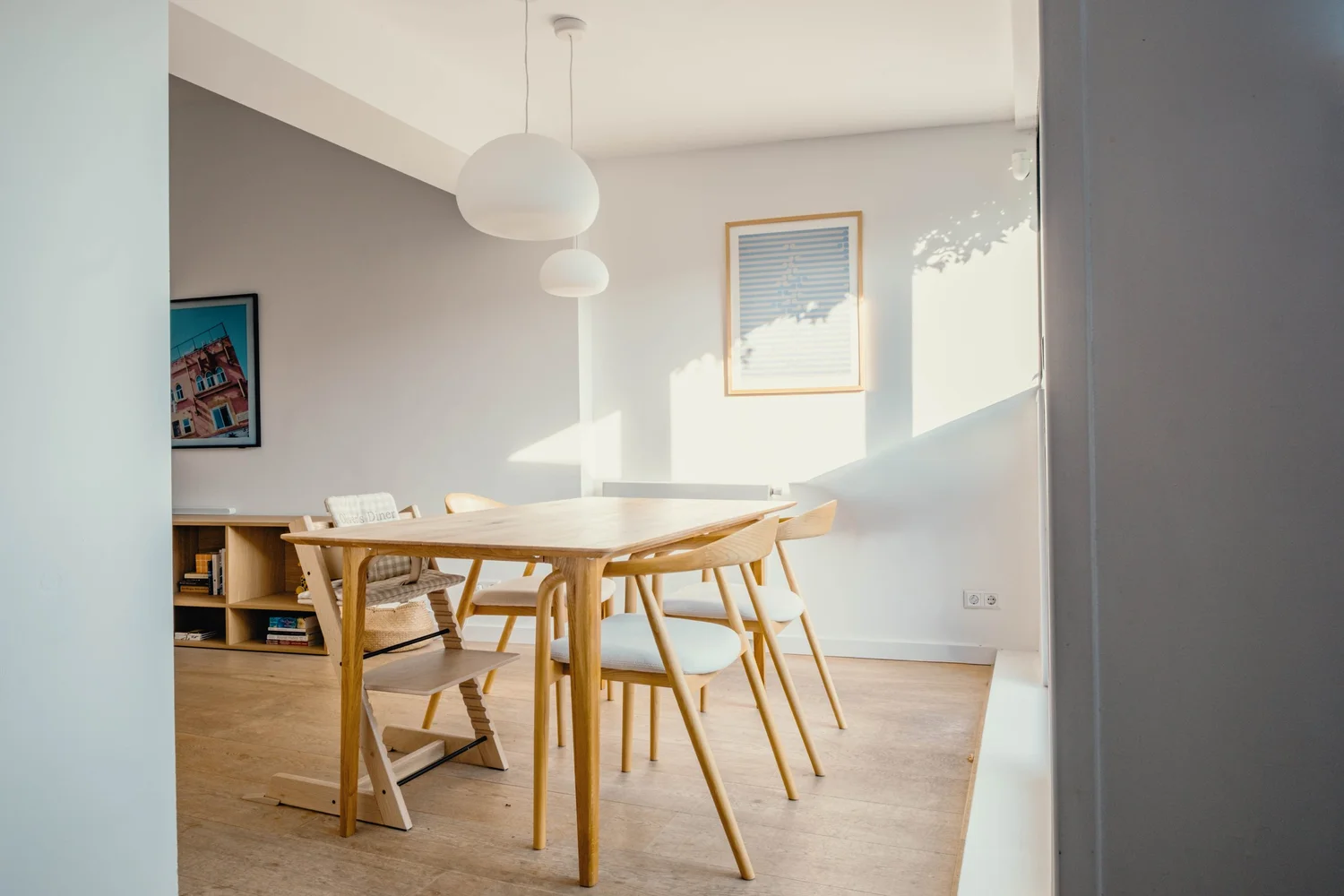 Lichte eetkamer met een houten tafel en witte eetstoelen.