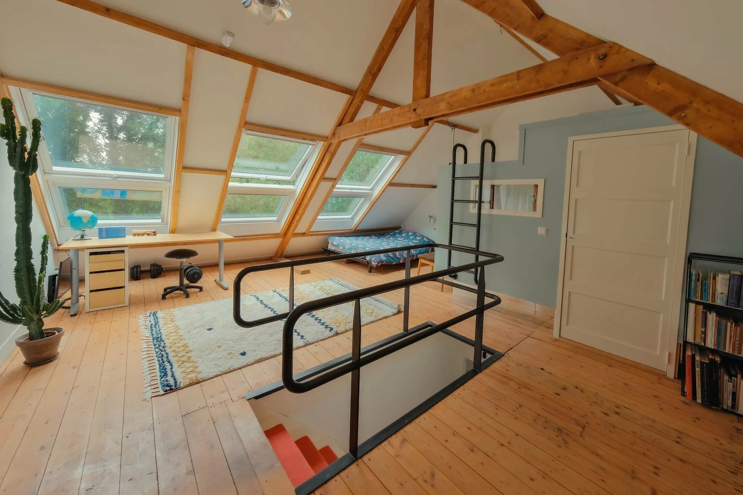 Zolderkamer met houten balken en drie schuiframen.