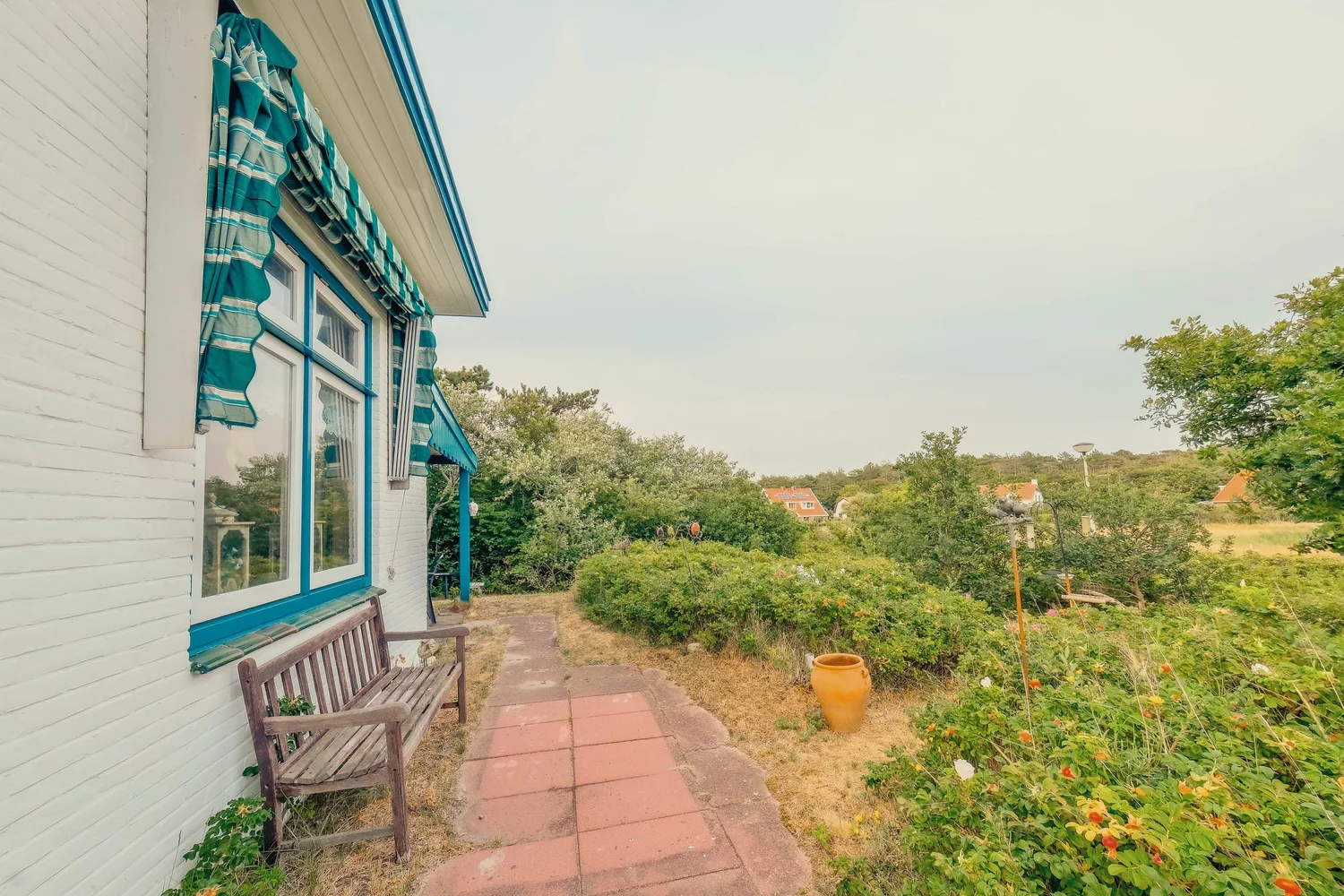 Wit huis met blauwe raamdecoraties, een grindpad en een tuin.