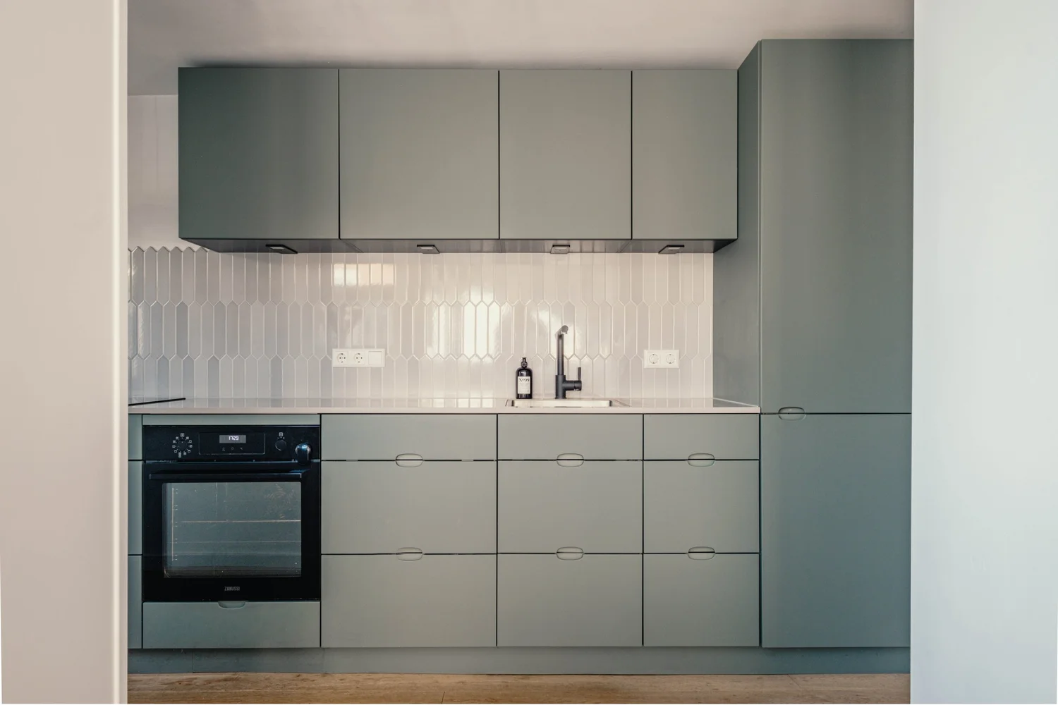 Moderne keuken met grijze kastdeuren en een witte hexagonale tegelwand.