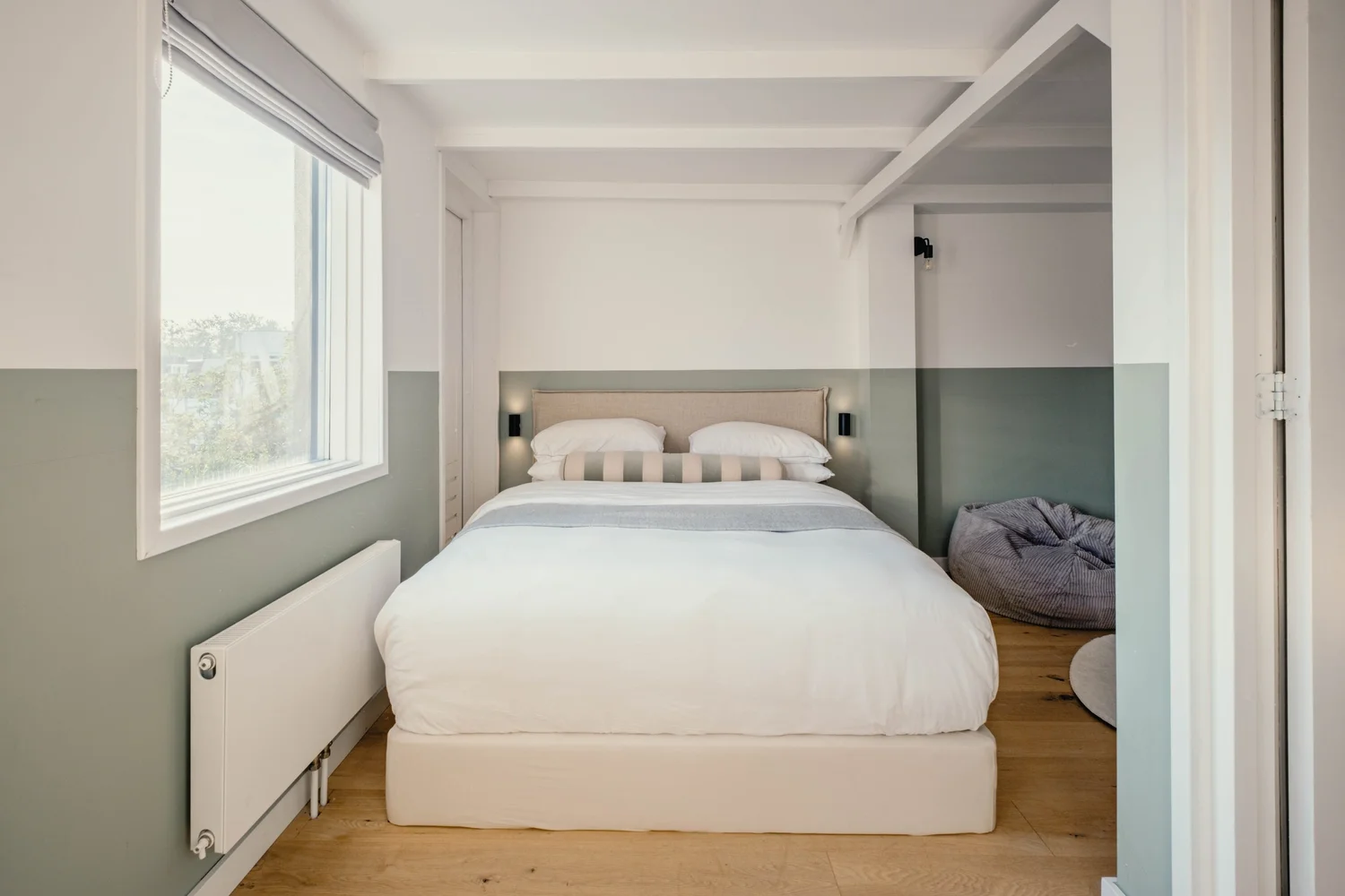 Slaapkamer met wit bed, beige hoofdeinde en wandlampen.