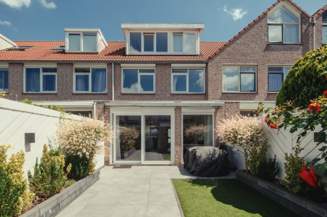 Achtertuin van een bakstenen huis met grote glazen deuren.