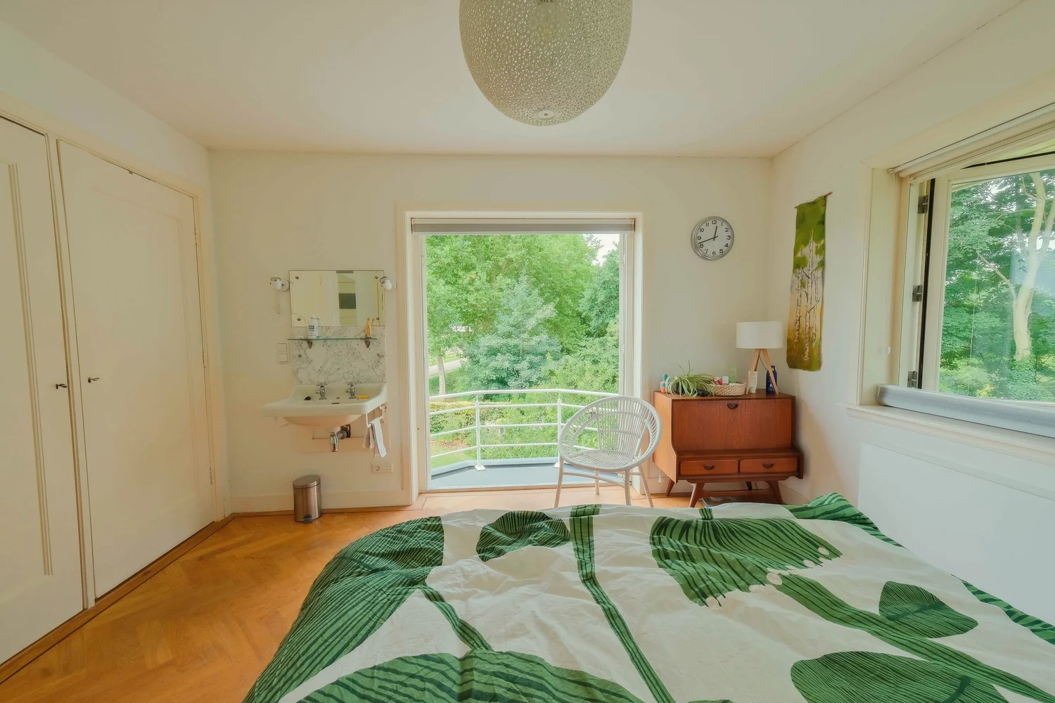 Slaapkamer met grote ramen en groen zichtbaar buiten.