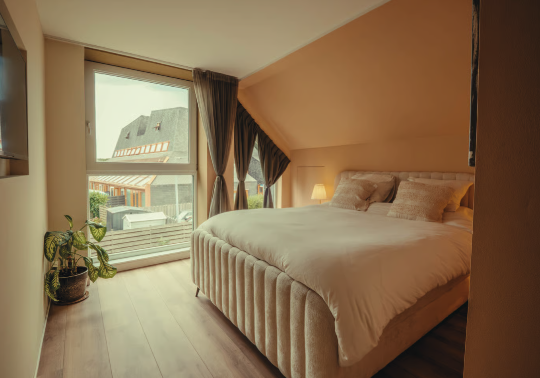 Slaapkamer met groot bed en uitzicht over de daken.