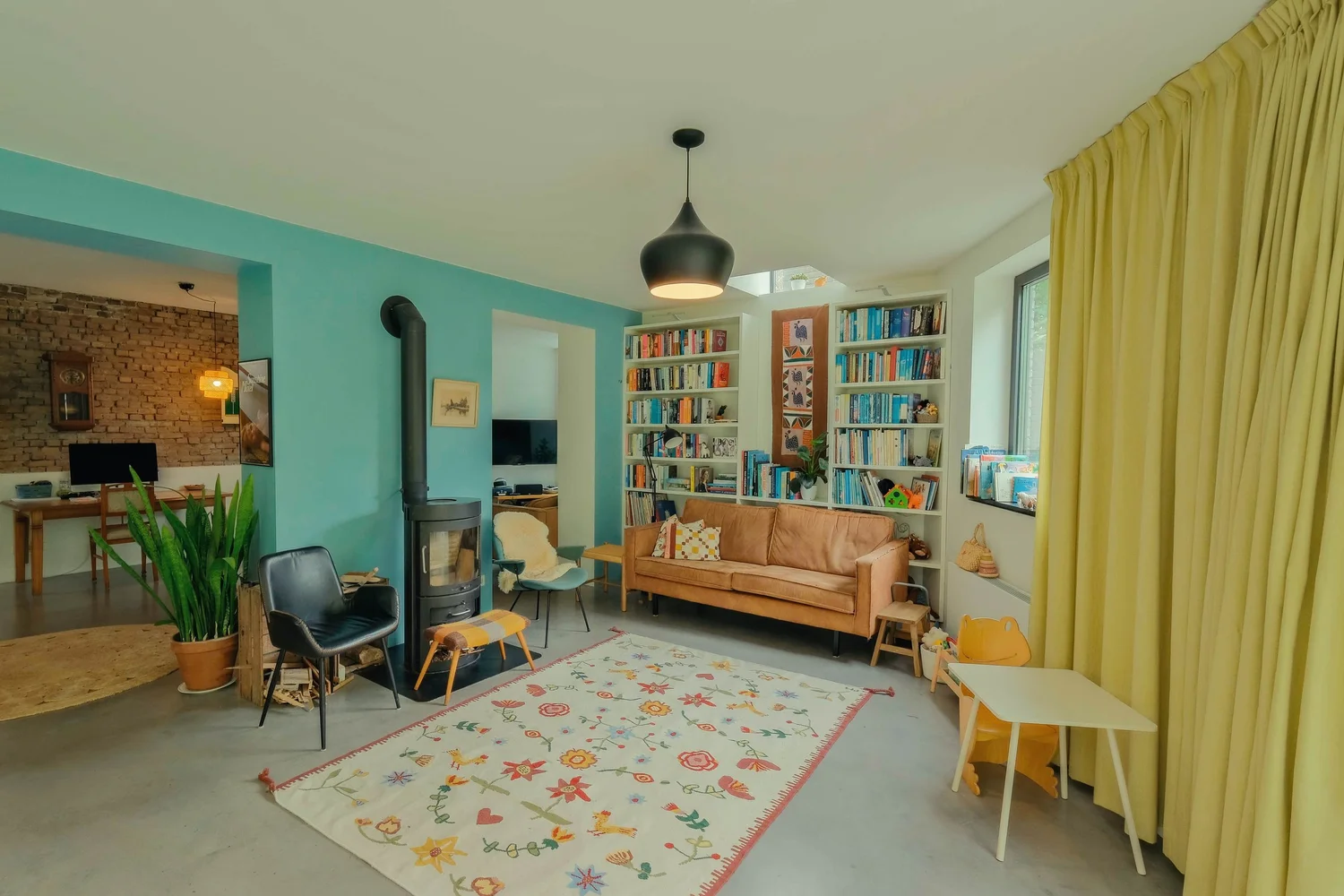 Woonkamer met een oranje bank, boekenkasten en gele gordijnen.