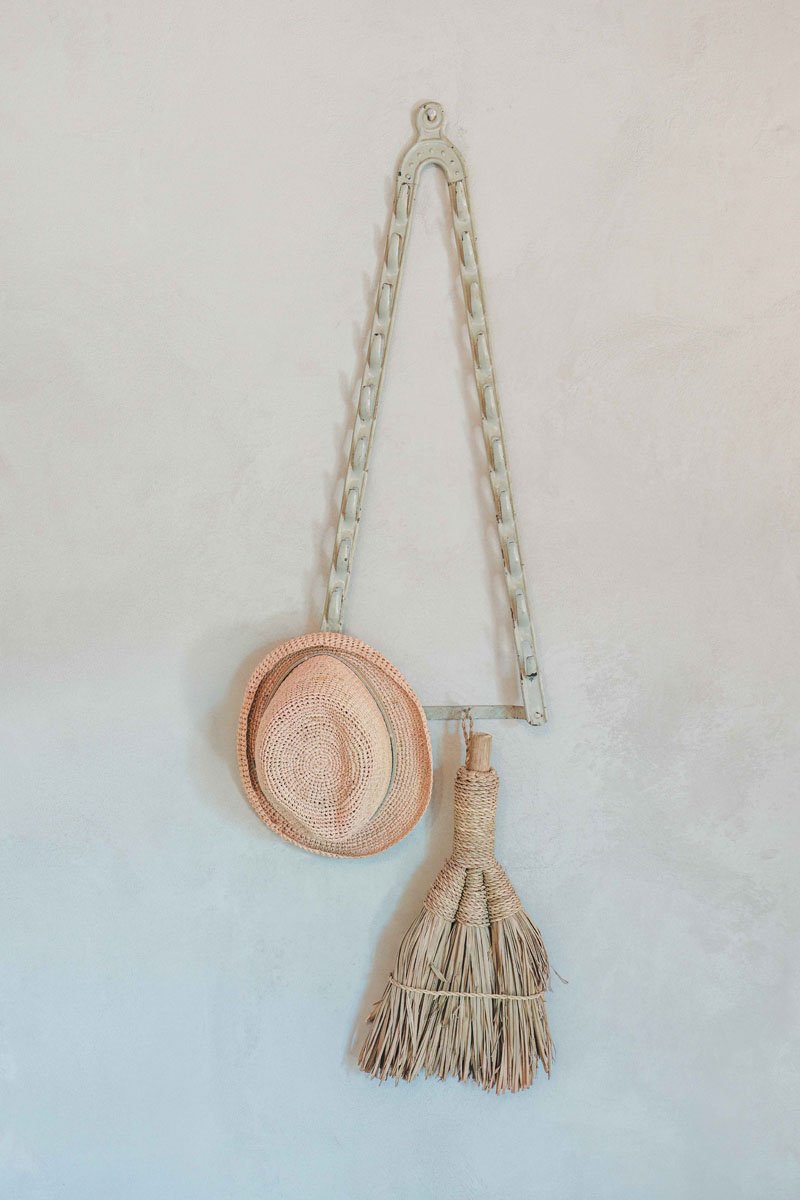 Decorative wall hanging with a woven pink hat and a straw broom on a white wall at Casa Janna. Luna Junior Suite interior
