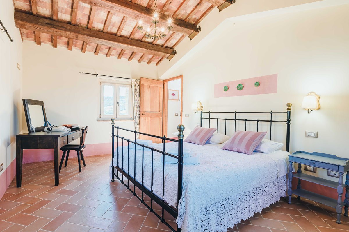 Bedroom at the Casa Janna Cottage with wrought iron bed, exposed wooden beams, and terracotta tile floor