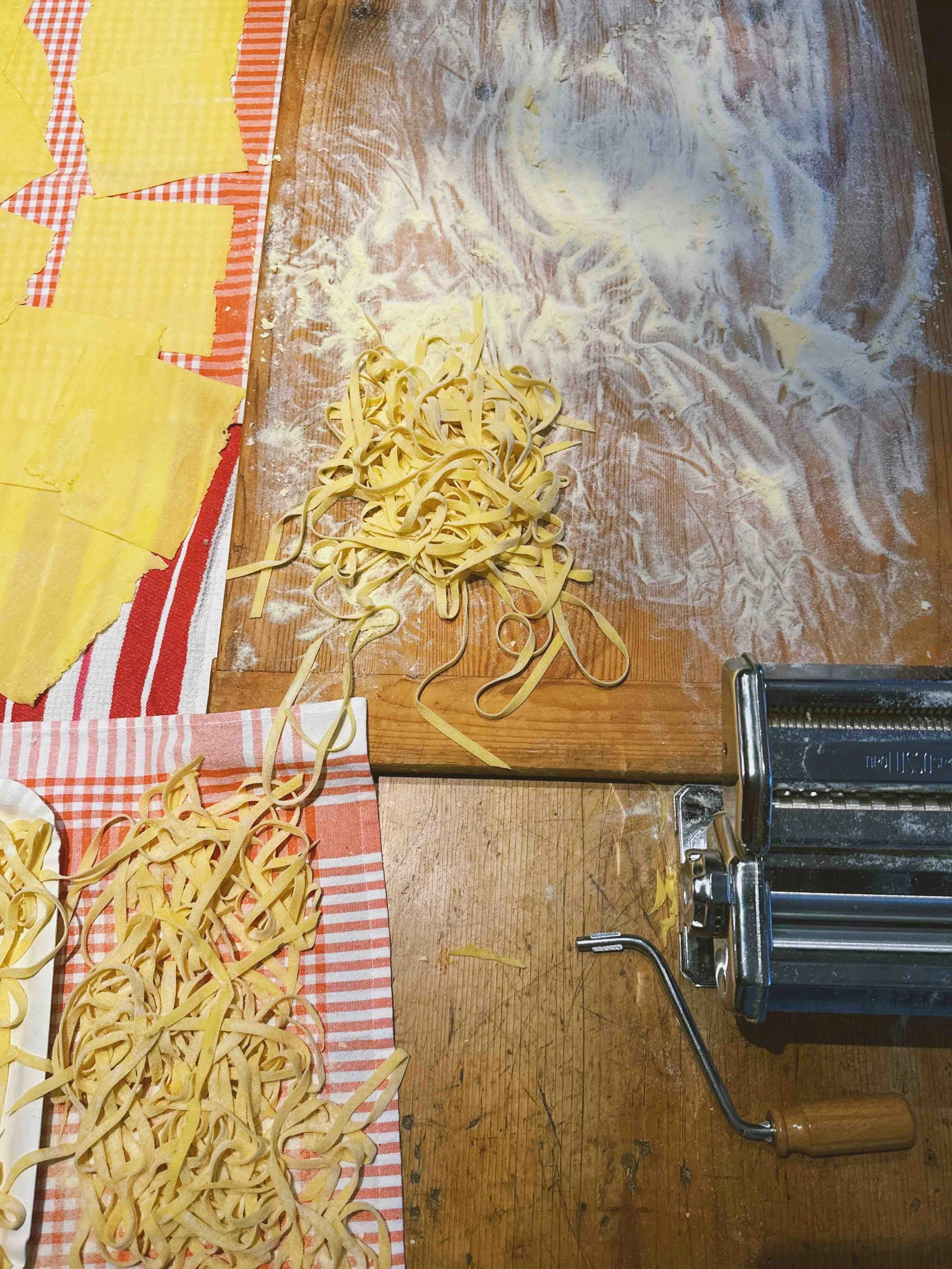 Uncooked pasta on a wooden surface with a pasta machine nearby.
