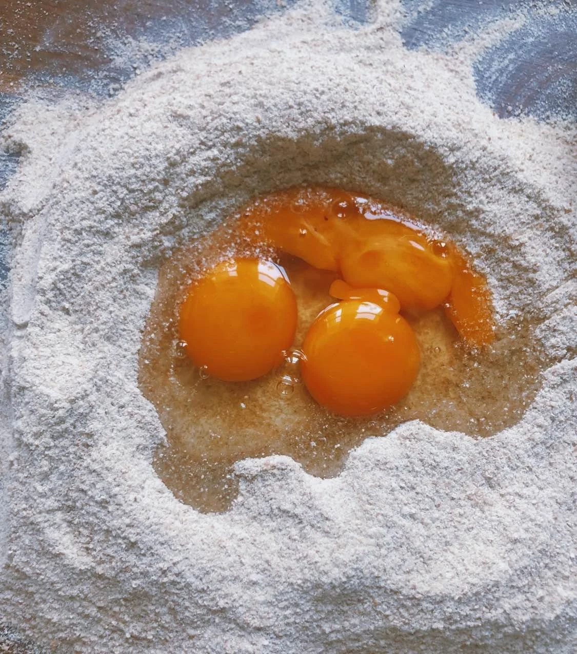 Flour on a surface with four cracked eggs in the center.