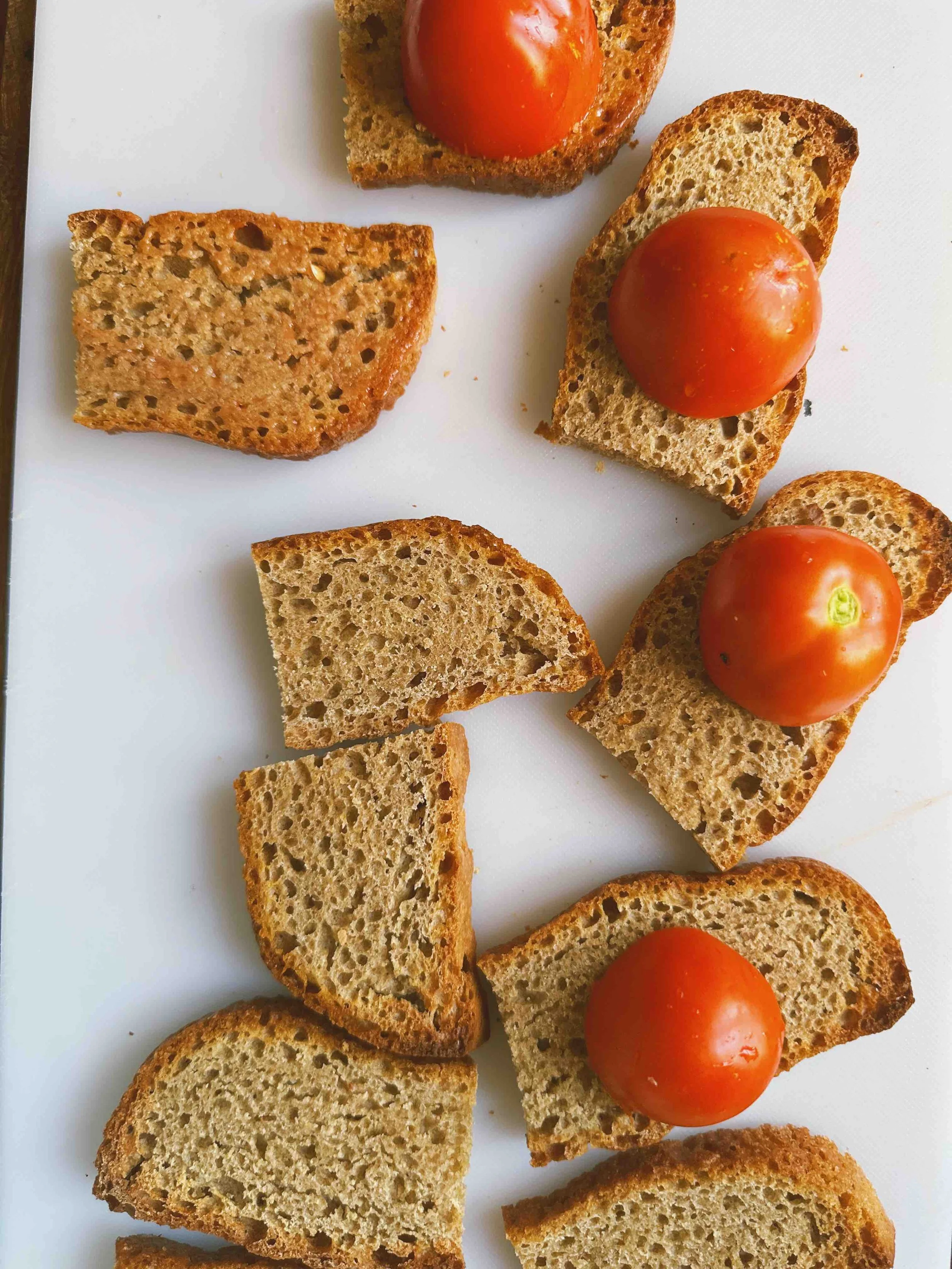 Slices of toasted bread topped with cherry tomatoes on a white cutting board.