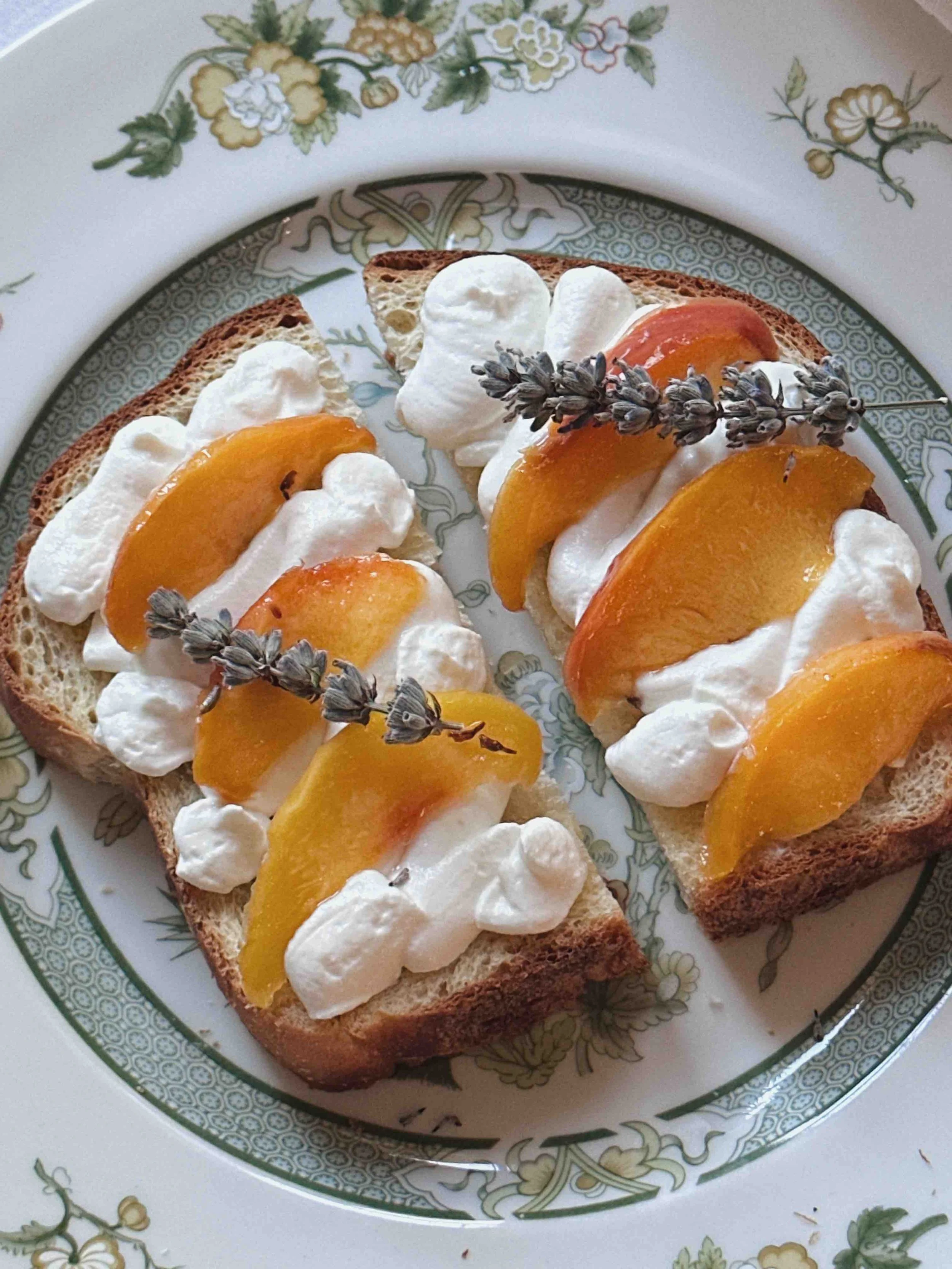 Two slices of bread topped with whipped cream, peach slices, and lavender sprigs on a decorative plate.