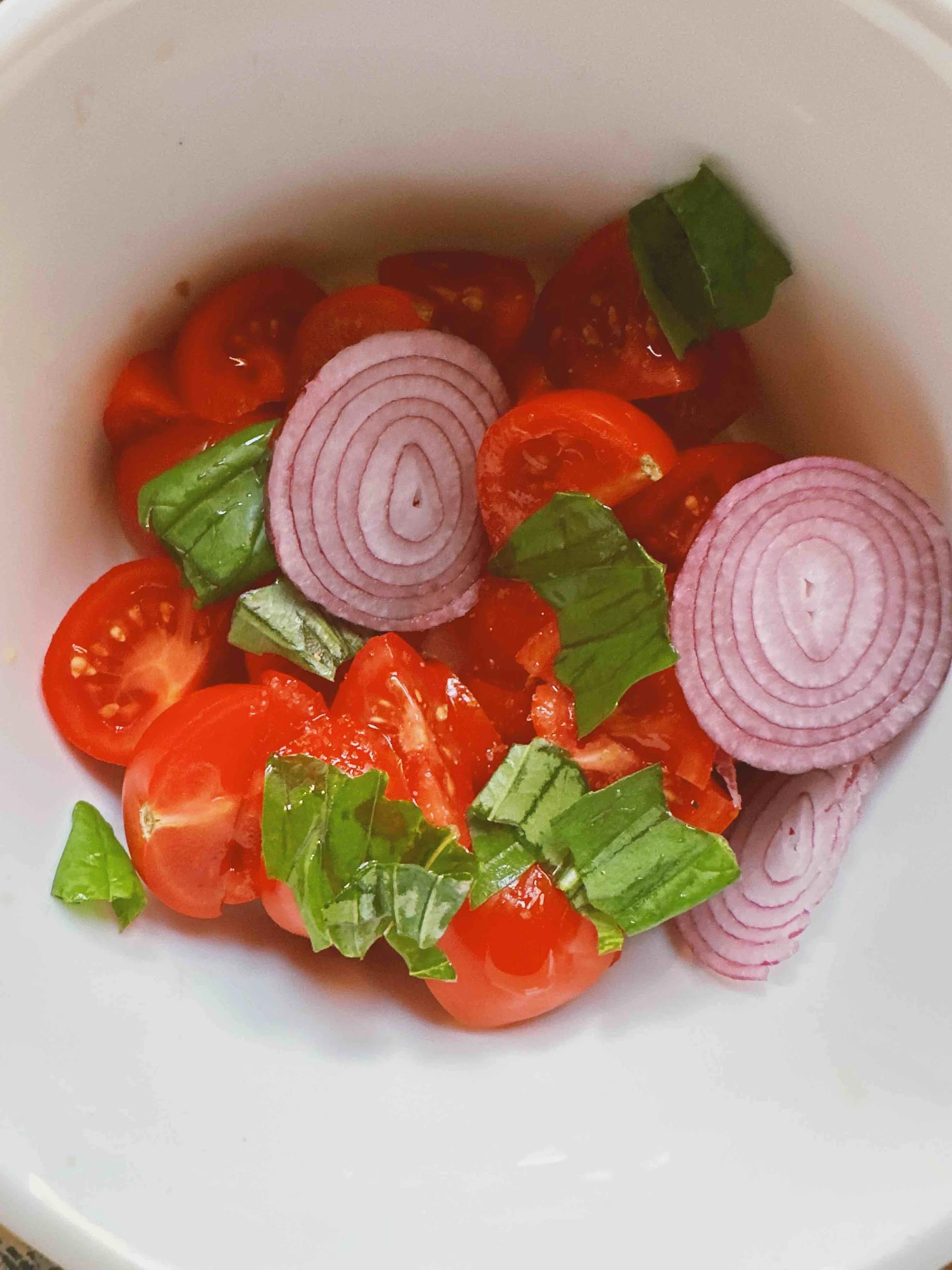 Cherry tomatoes, sliced red onions, and chopped green herbs in a white bowl.