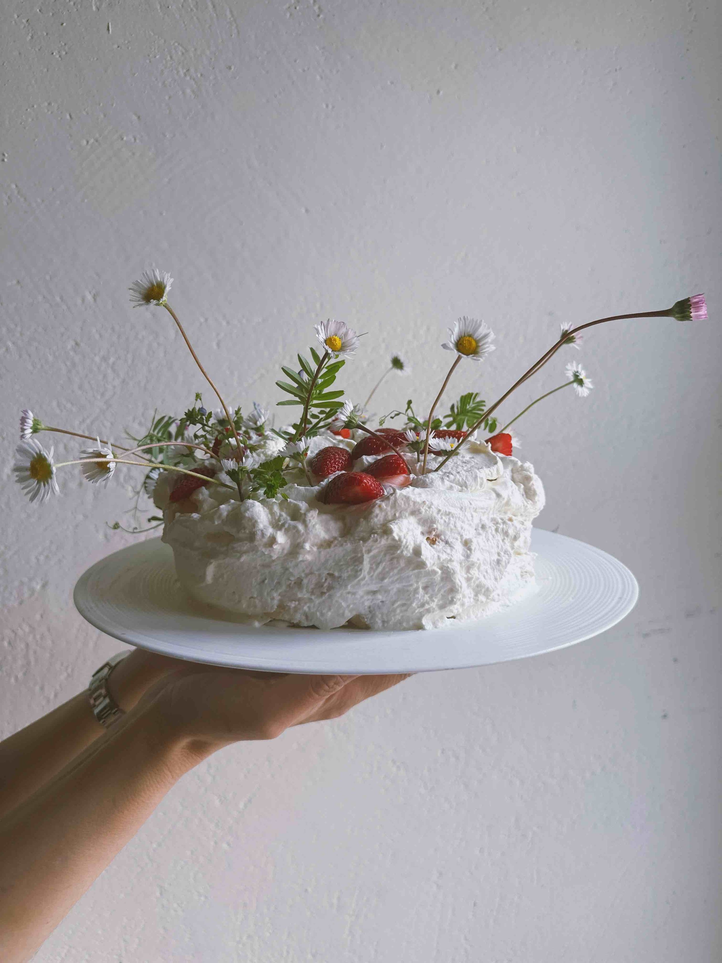 Cake decorated with strawberries, flowers, and greenery on a white plate