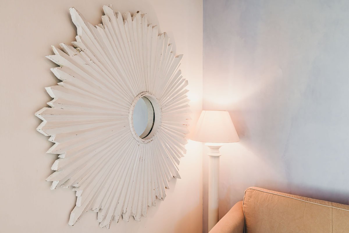 White sunburst mirror hanging above a sofa and floor lamp in a Casa Janna interior. Sole Junior Suite interior