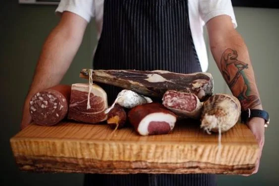 Person in apron holding a wooden charcuterie board.