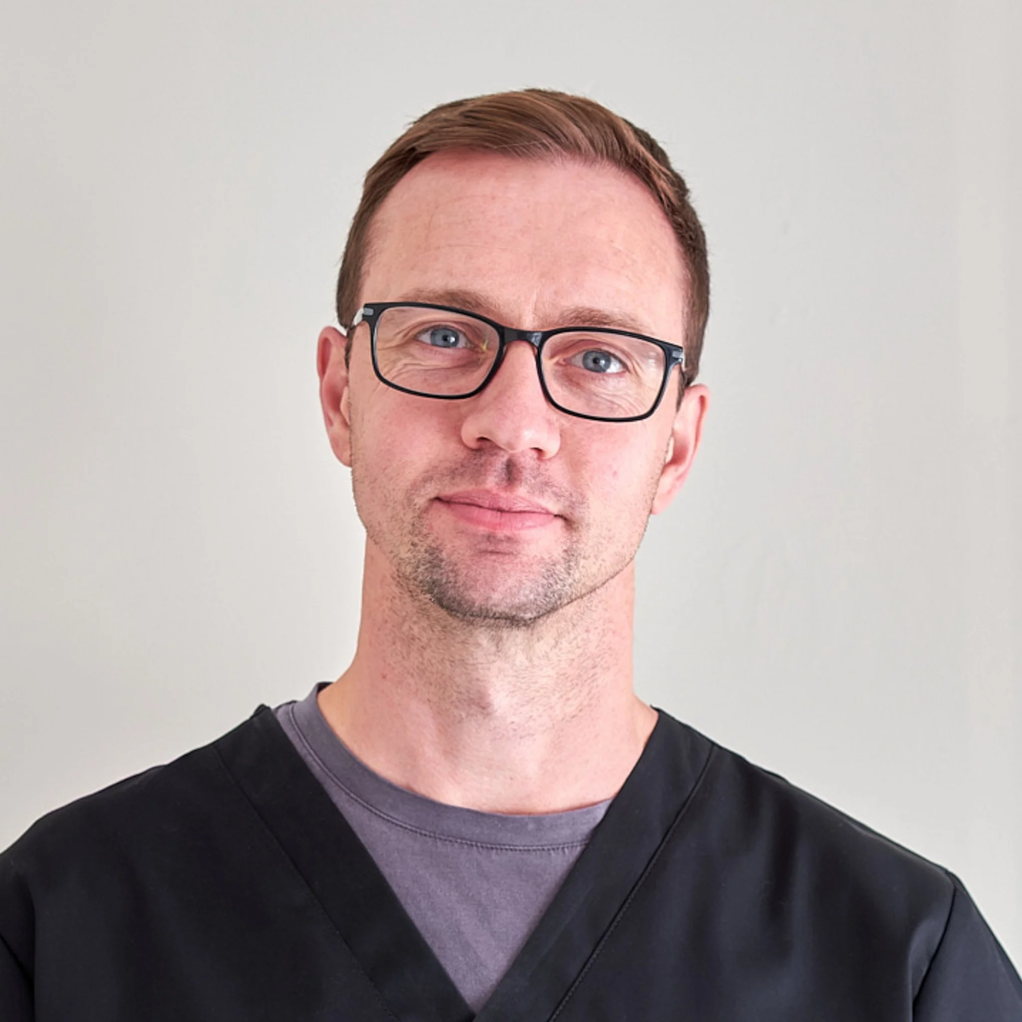 Close-up of a person's face showing the forehead, glasses, eyes, nose, mouth, and part of their neck and clothing against a plain background.