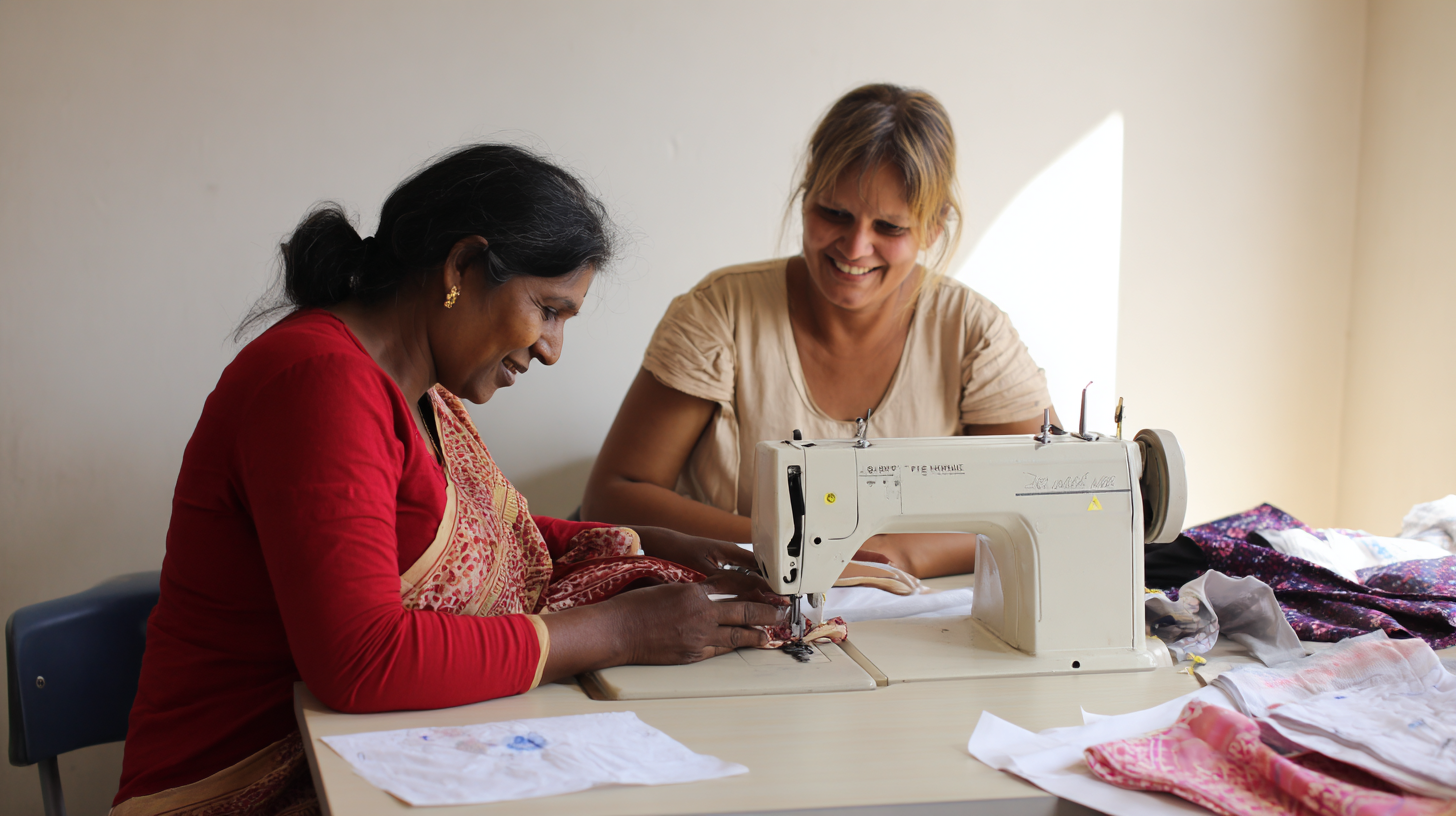 Deux femmes dans une pièce, l'une utilisant une machine à coudre et l'autre souriant. Autour d'elles, du tissu et du papier sur la table.