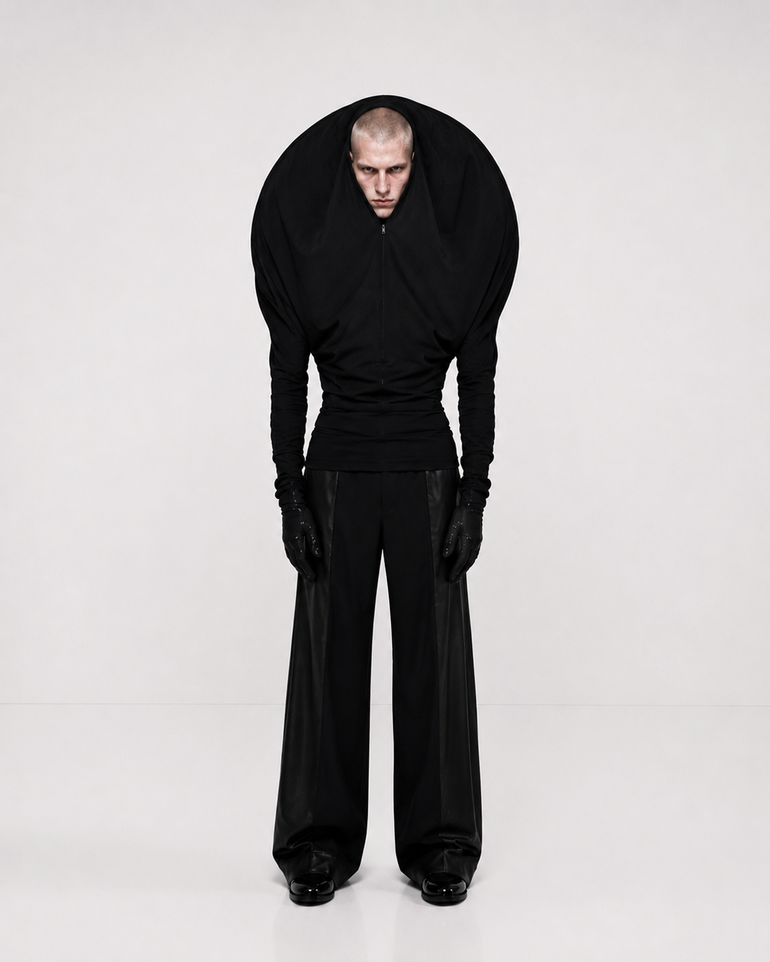 Model wearing an all-black sculptural fashion look with exaggerated shoulders against a white background.