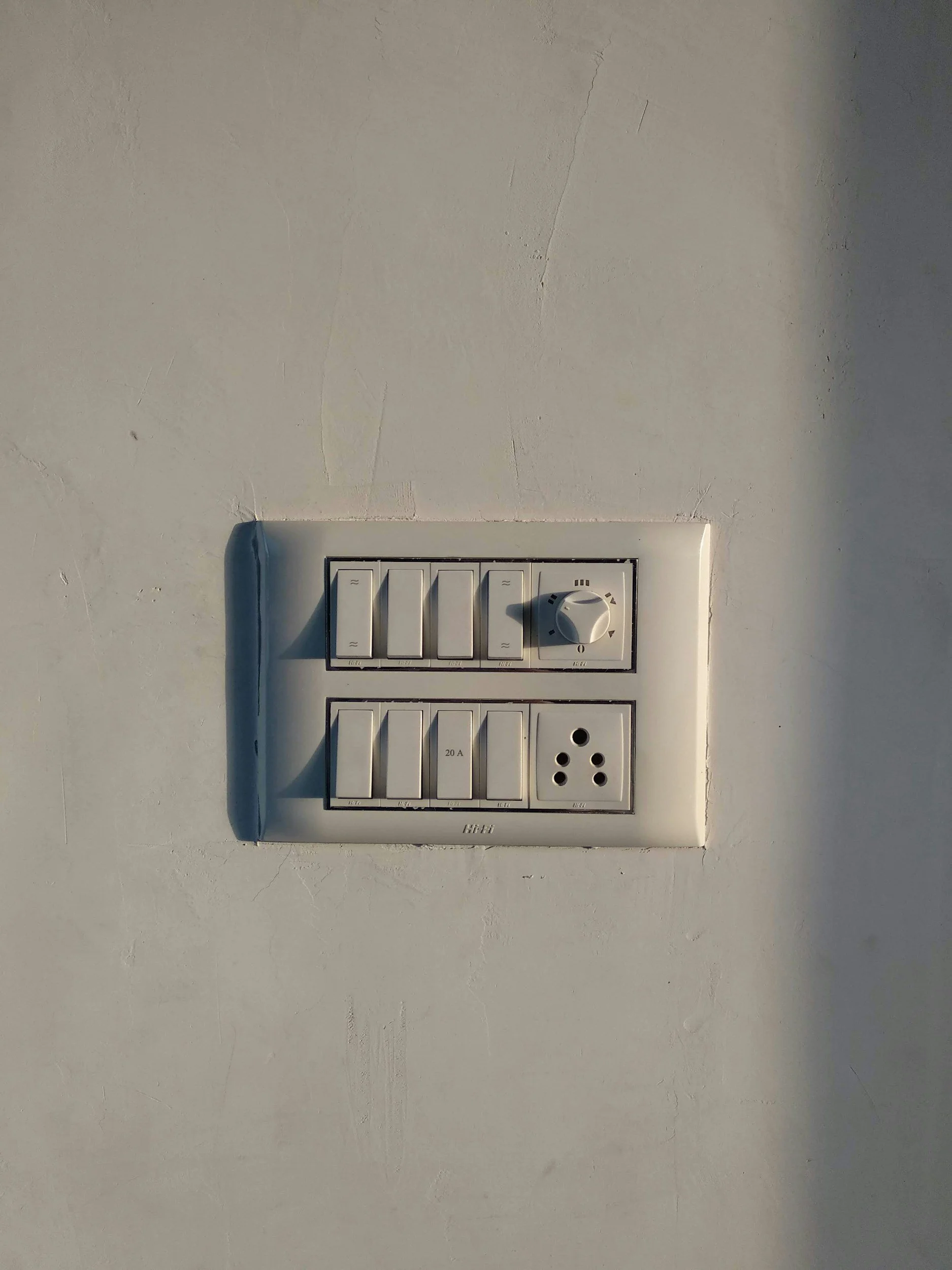 Electrical wall switch panel with multiple switches and a dial, mounted on a white wall.