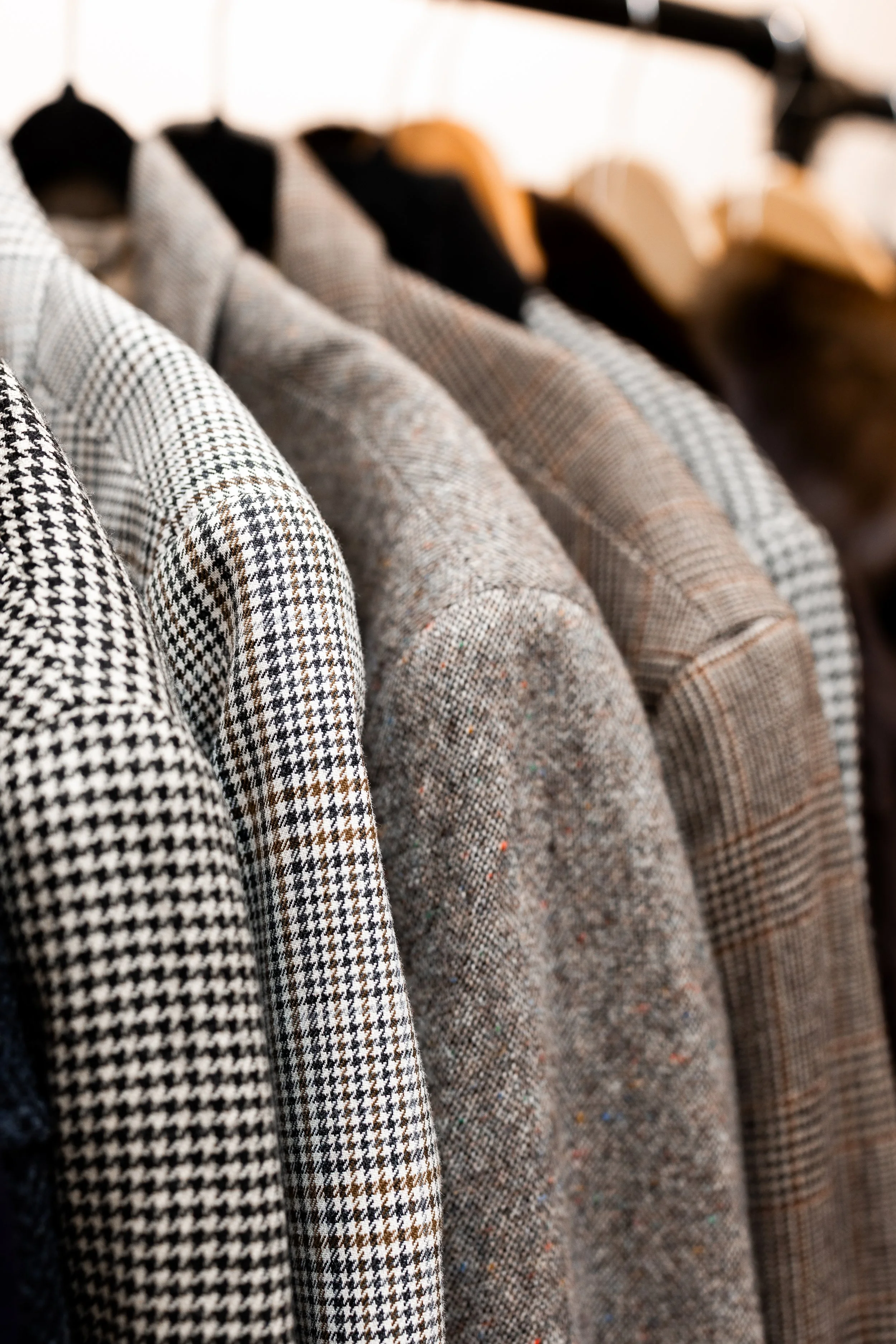 A row of men's jackets hanging on a rack, featuring various plaid and checkered patterns in neutral tones.
