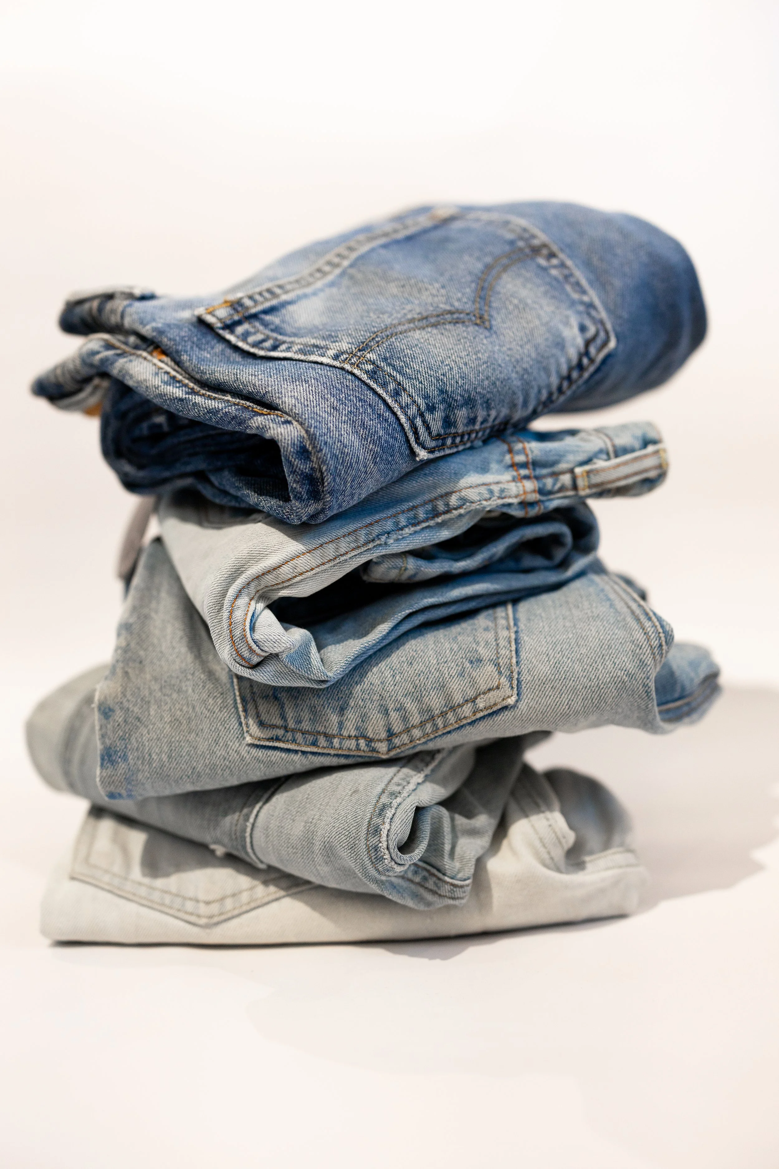 Stacked folded jeans in various shades of blue and gray on a white background.