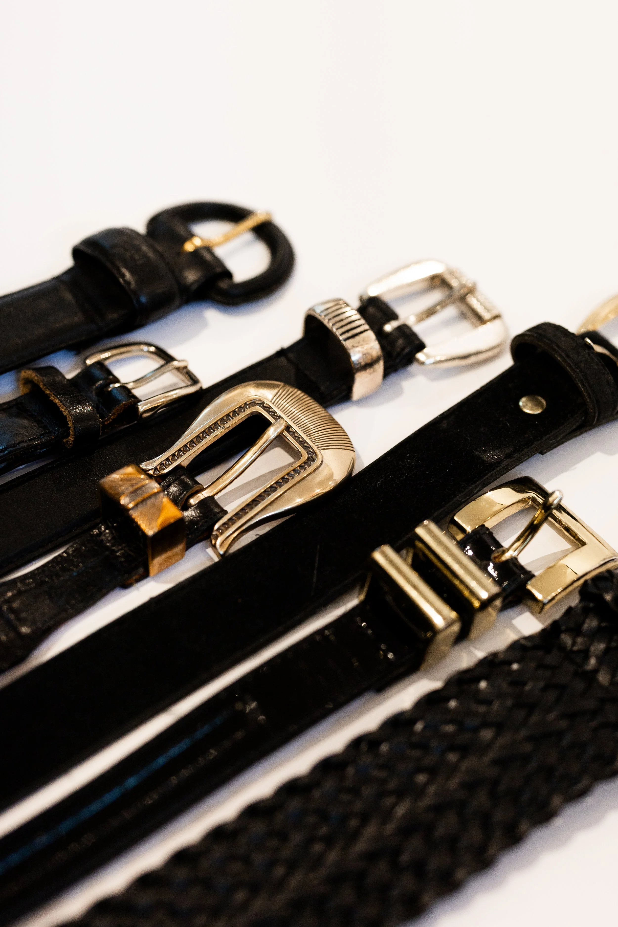 Close-up of black and gold belts with various buckles arranged on a white surface.