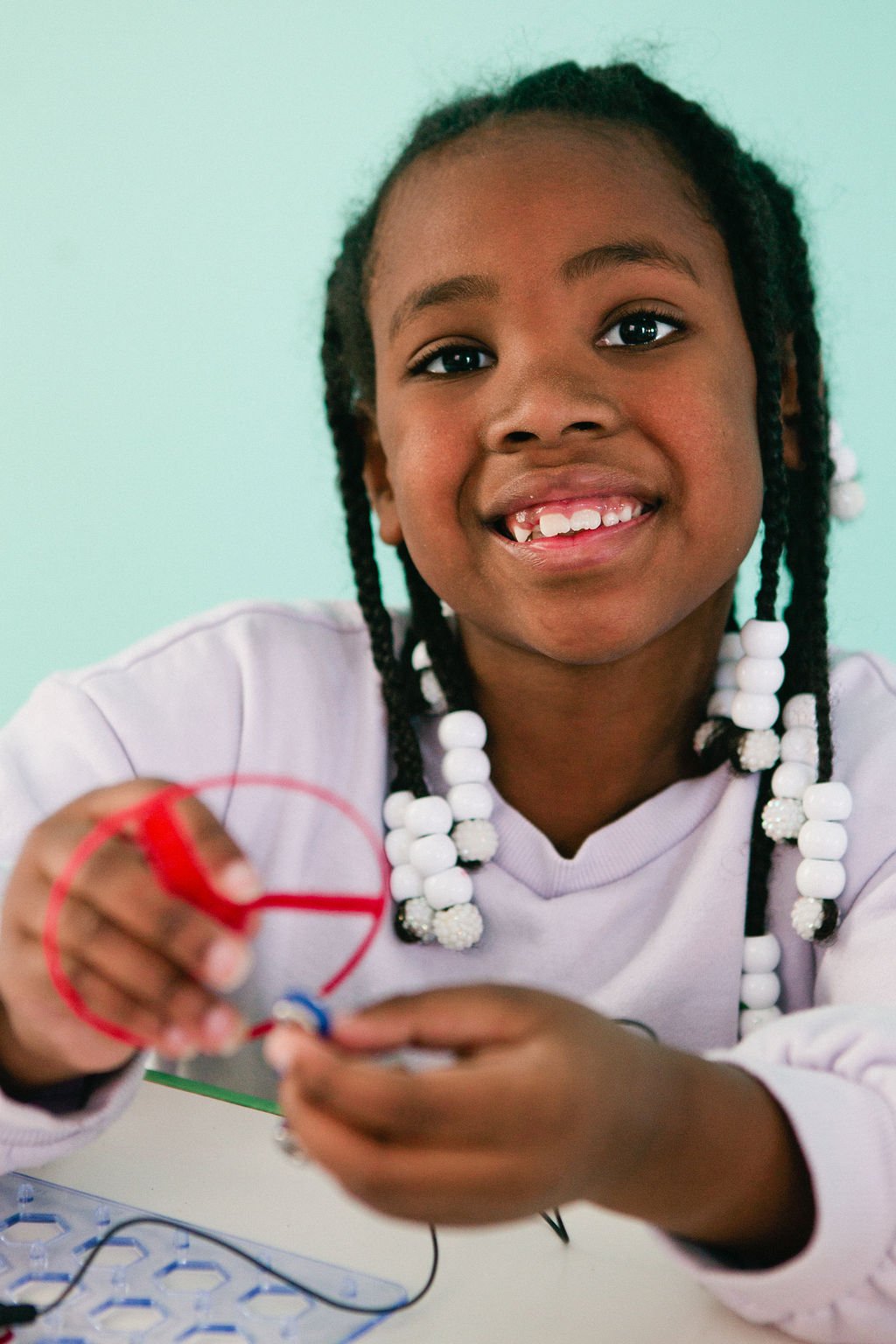 Young girl smiling while working on a science project with a resistor and circuit board.