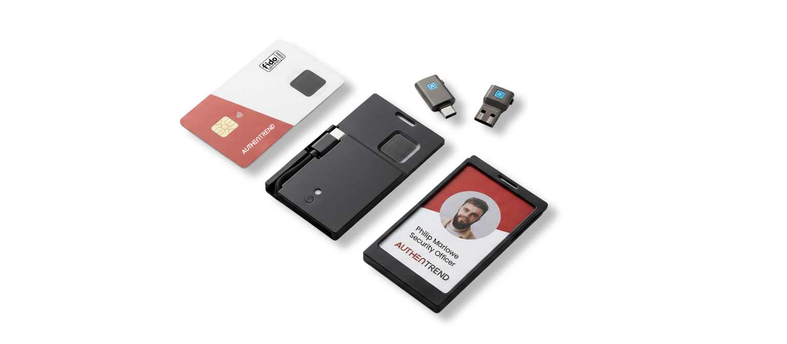 Digital ID badge displaying a man's photo, name, and title, along with a proximity card, a portable fingerprint scanner, two USB adapters, and a black case placed on a dark surface.