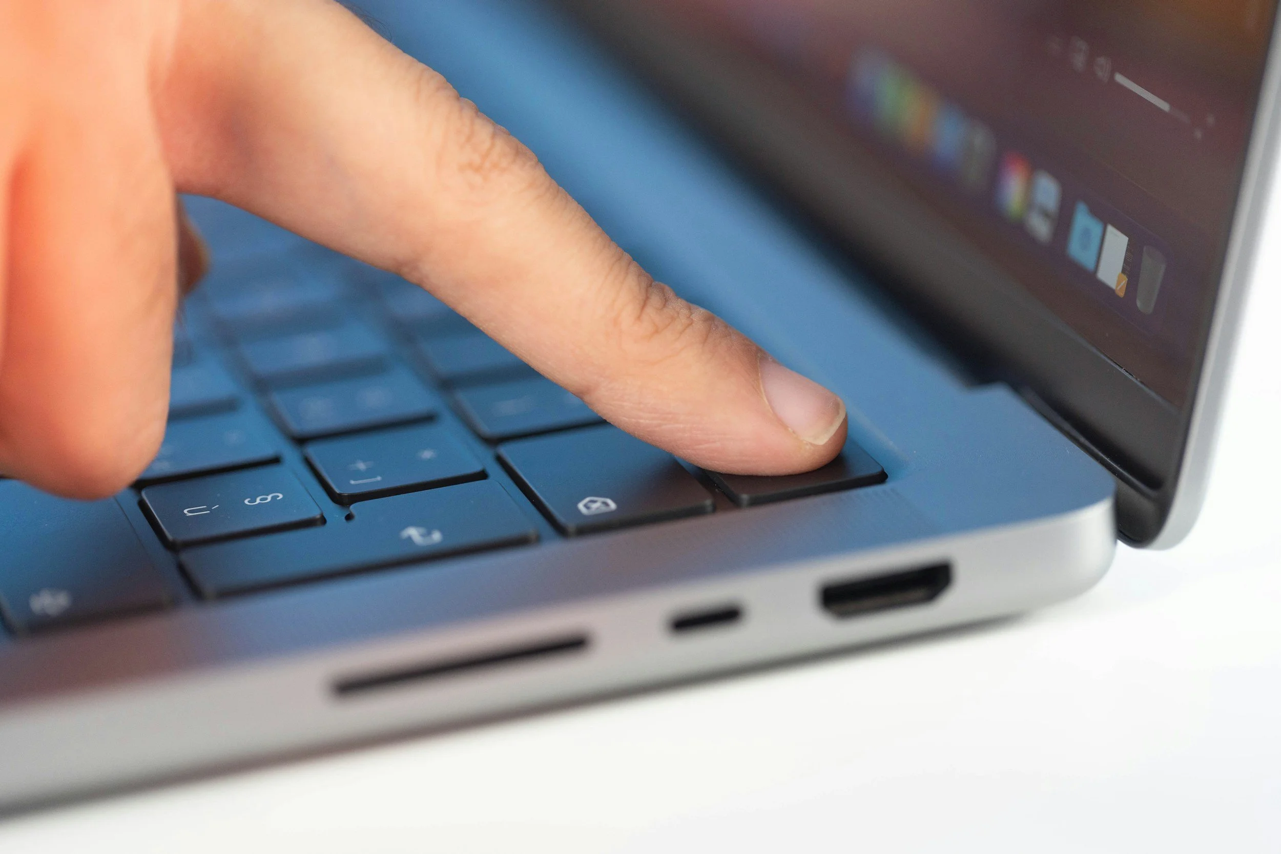 Close-up of a person's finger pressing a key on a laptop keyboard, with a computer screen in the background.