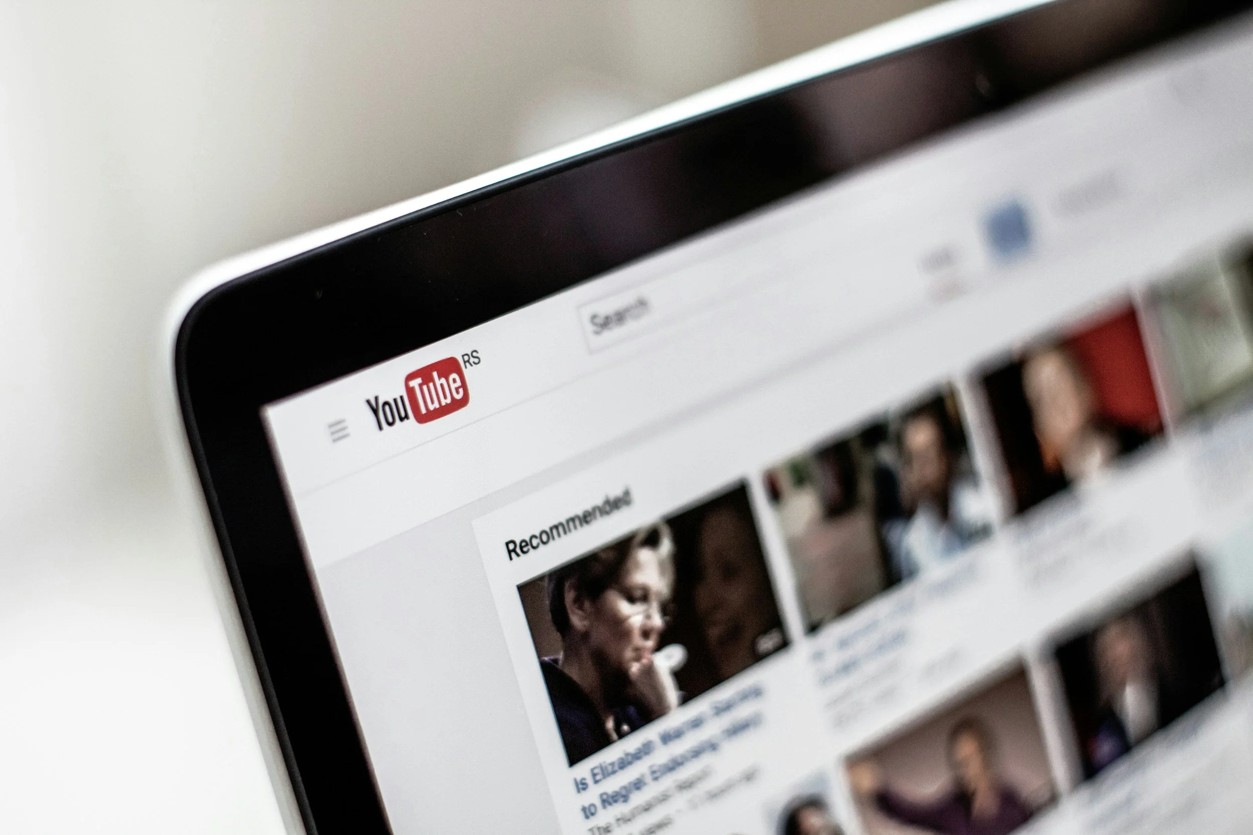 Close-up of the top left corner of a laptop screen displaying the YouTube homepage, with the logo and part of the recommended videos section.