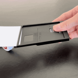 Person inserting a SIM card into a black electronic device, possibly a smartphone or tablet, on a dark surface.