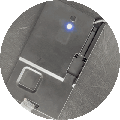 Electronic device with a blue LED light on, and a metallic surface, placed on a textured gray surface.